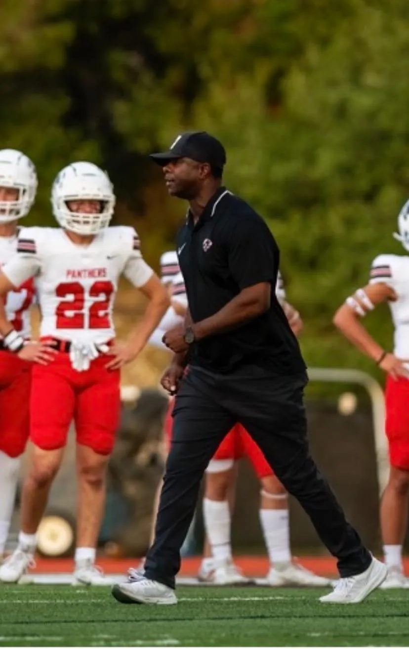 Coach mentoring a group of young football players on a field at sunset
